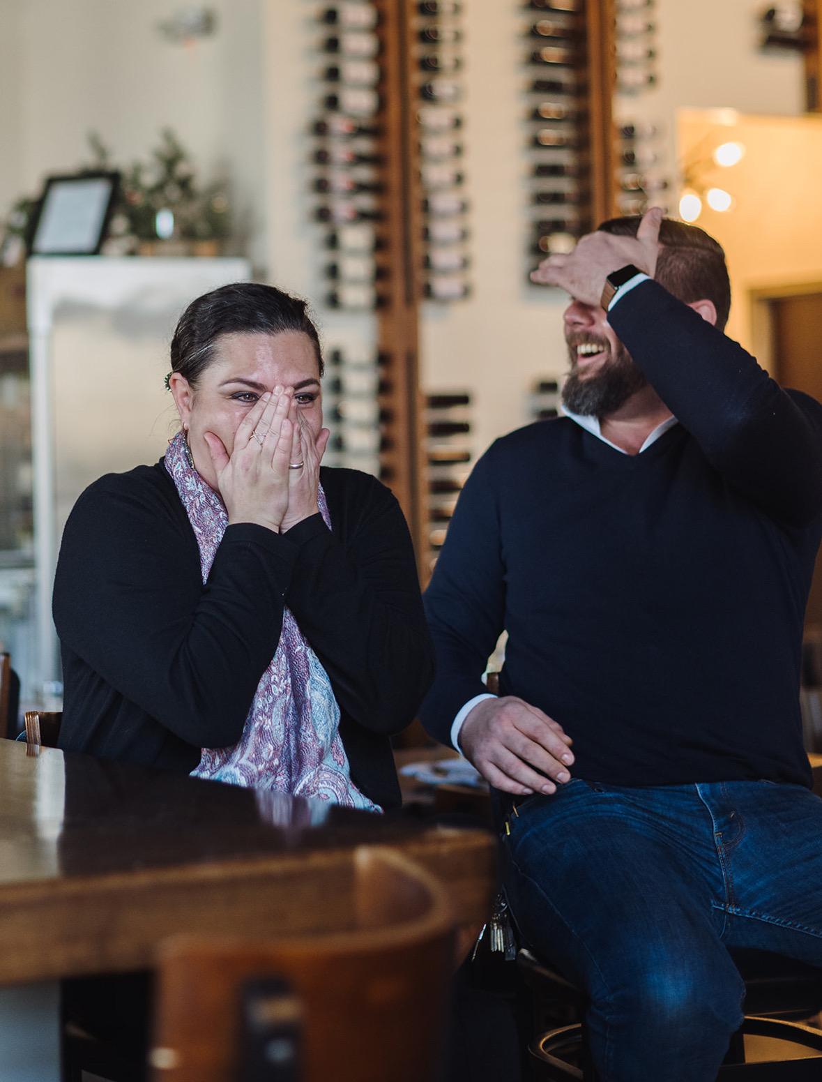 Two people seated, smiling in surprise.