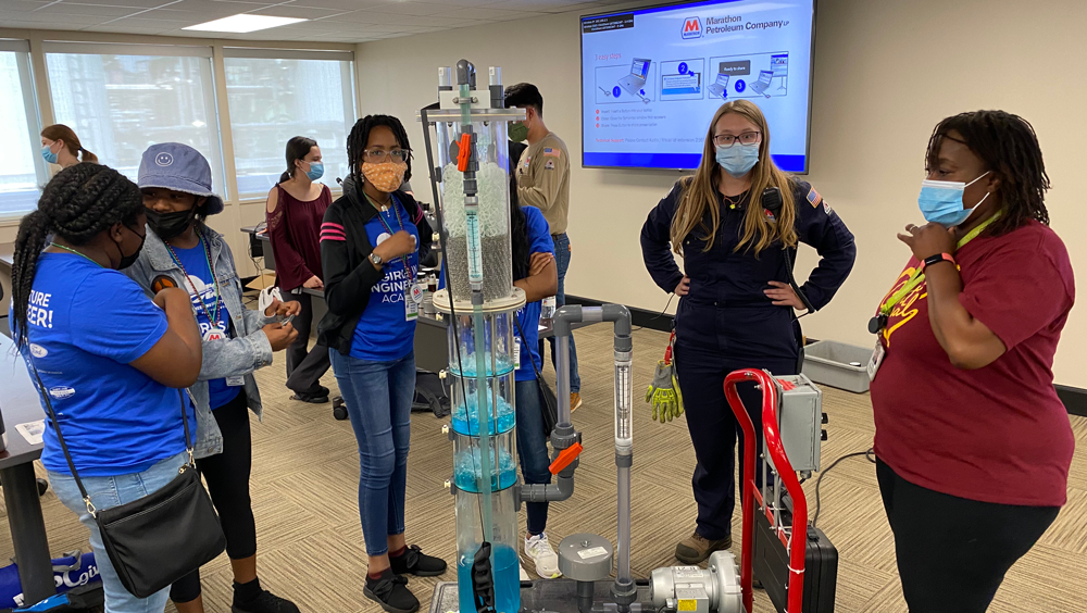 a group of people standing around a model of a distillation tower