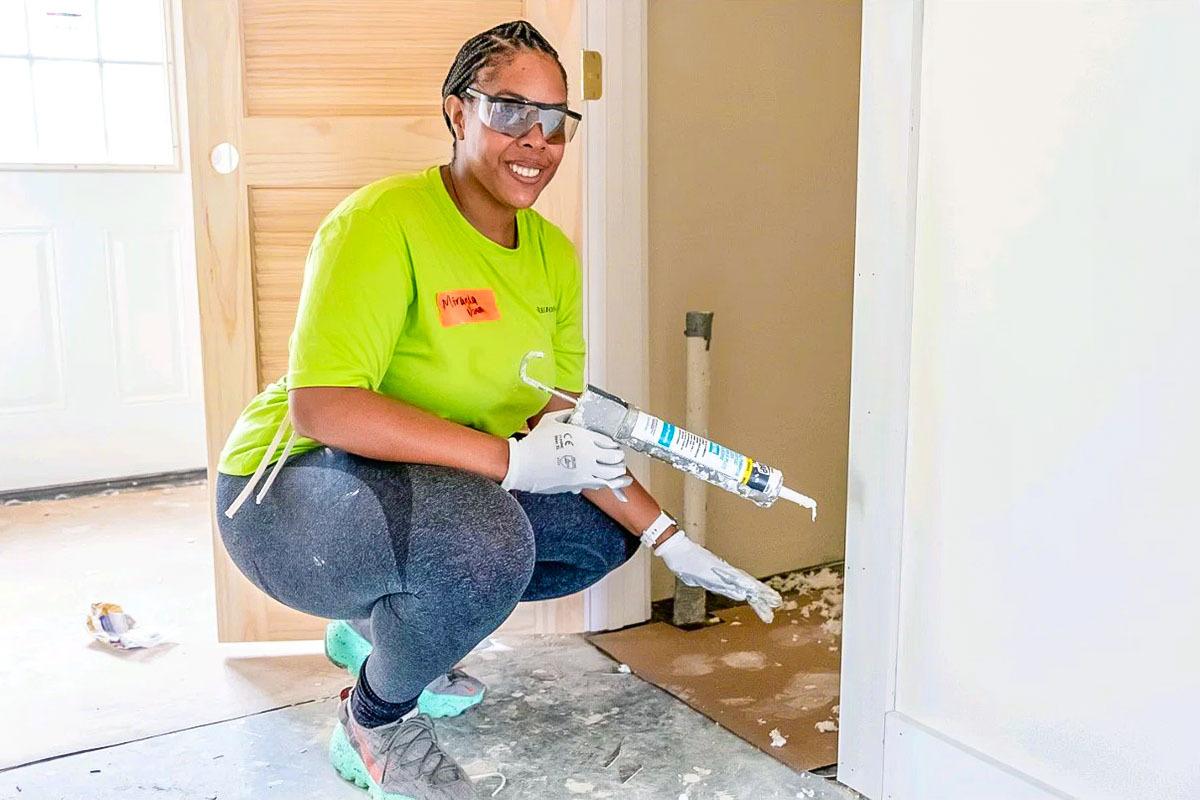 A smiling volunteers holding a caulk gun.