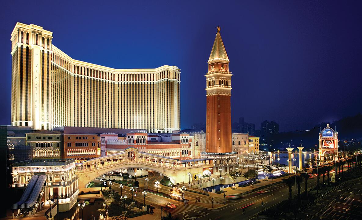 Aerial view of the exterior of a large tower in front of a resort at night.