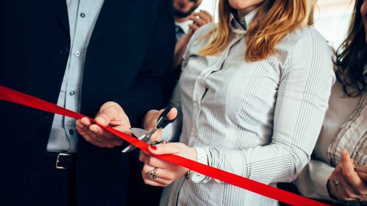 A person cutting a red ribbon with scissors, people on both sides of them.