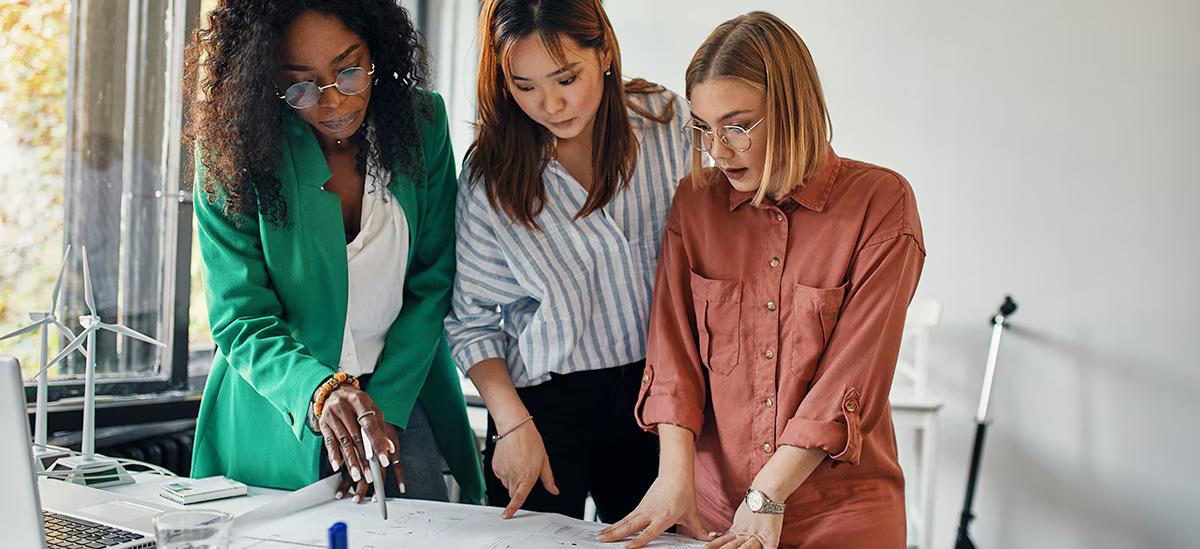 Three women stood at a desk looking at a piece of paper 