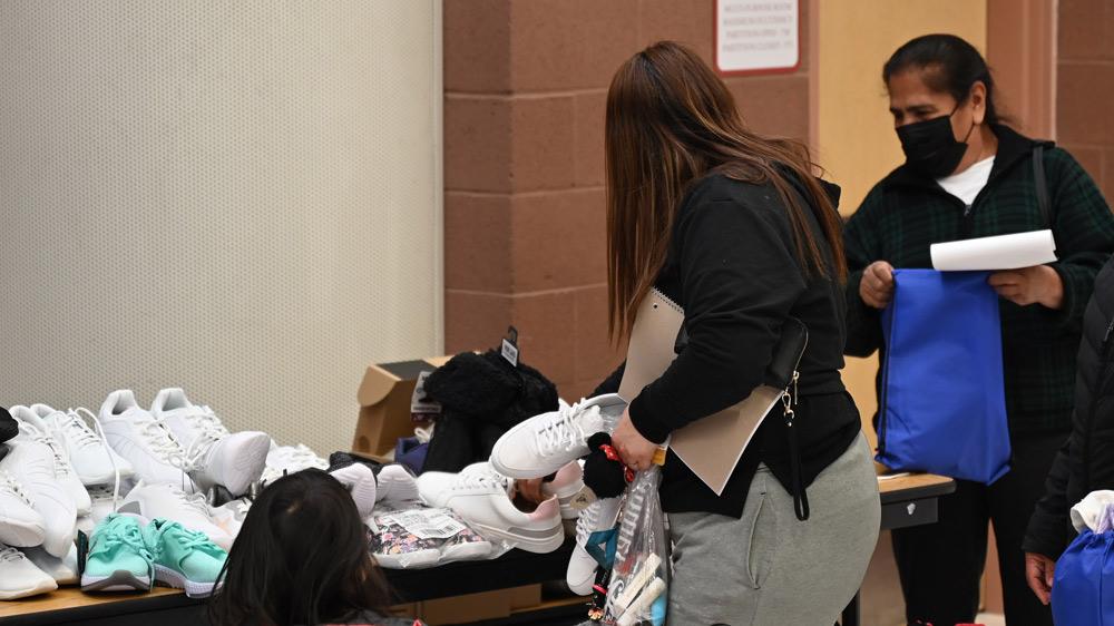 a person takes a pair of shoes from a table with many identical pairs and other clothing items on it.