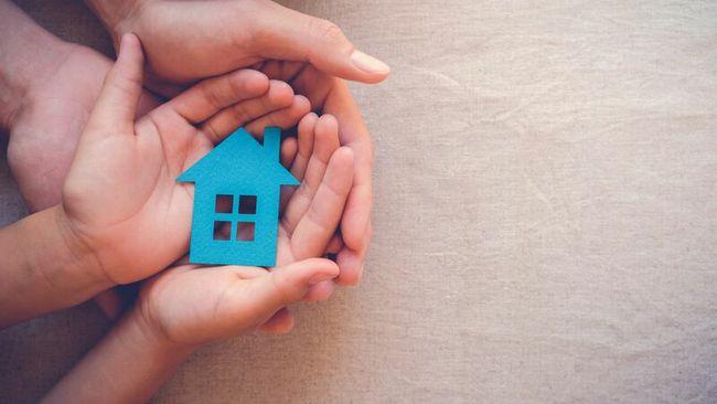 A child resting their hand on top of an adults palm, holding a little blue house figure