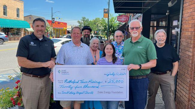 A group of people posed with a large check on a sidewalk.