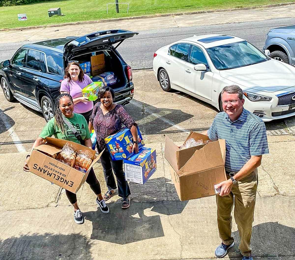 a group of four people unloading snacks and food from the back of a car