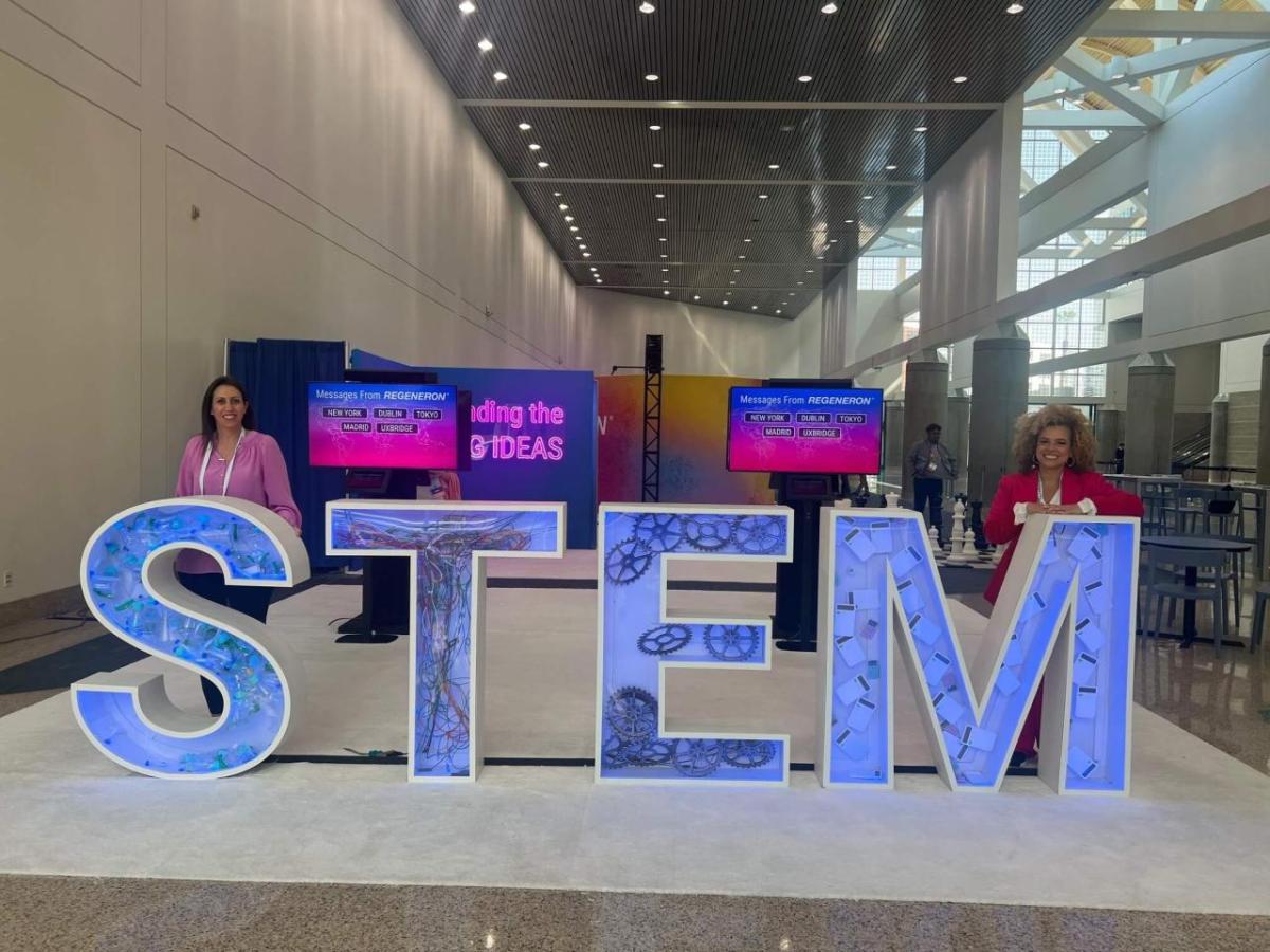 Two people standing behind large letters "S T E M".