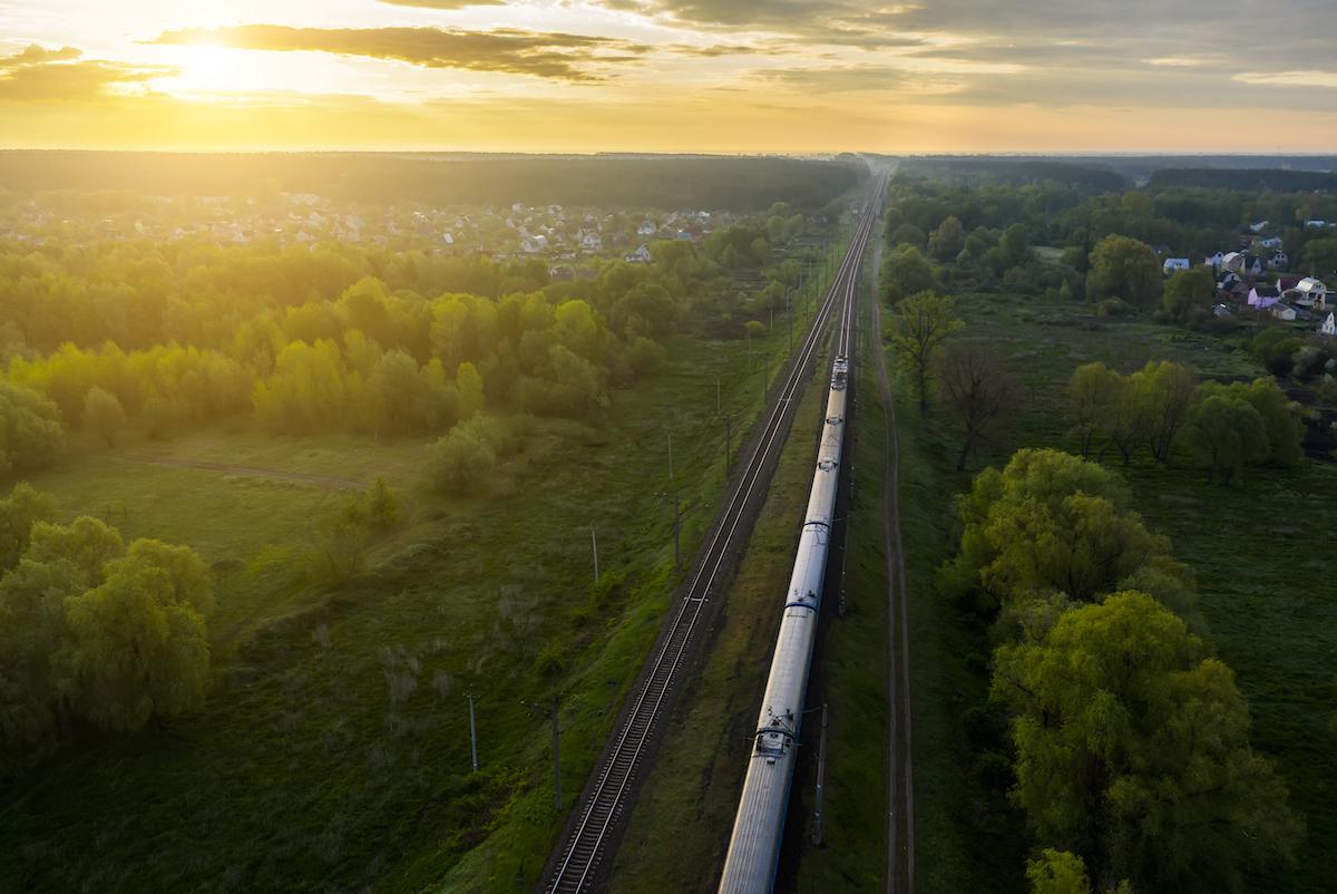 a long train moving through a green landscape at dawn