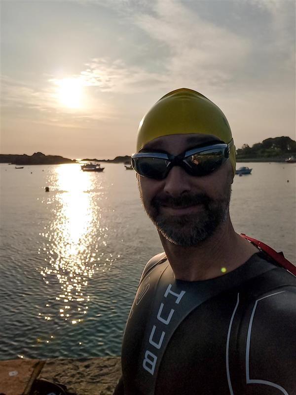 A person in a swim cap, goggles, and wet suit next to a body of water.