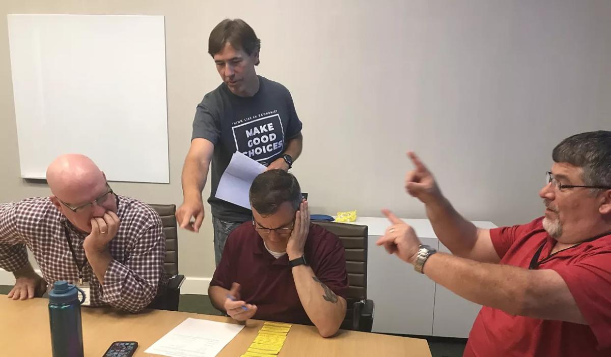 three people sitting, looking at a list and one behind them pointing