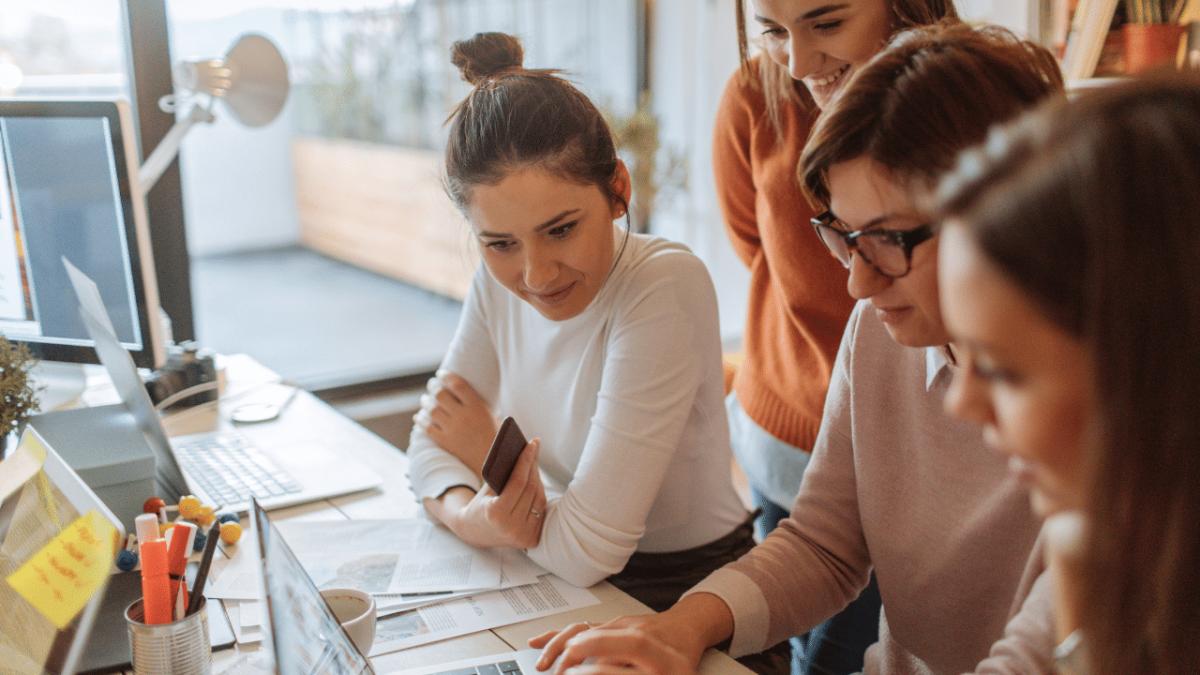 a group of four people looking at the same laptop on a desk