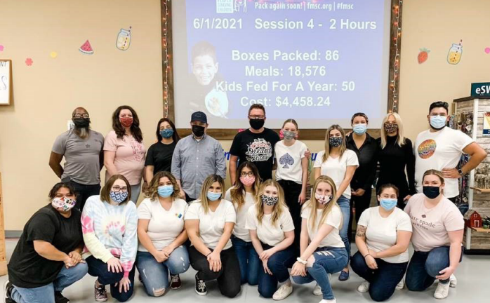 a group posed in front of a projected screen with stats of meals, cost, kids helped, etc