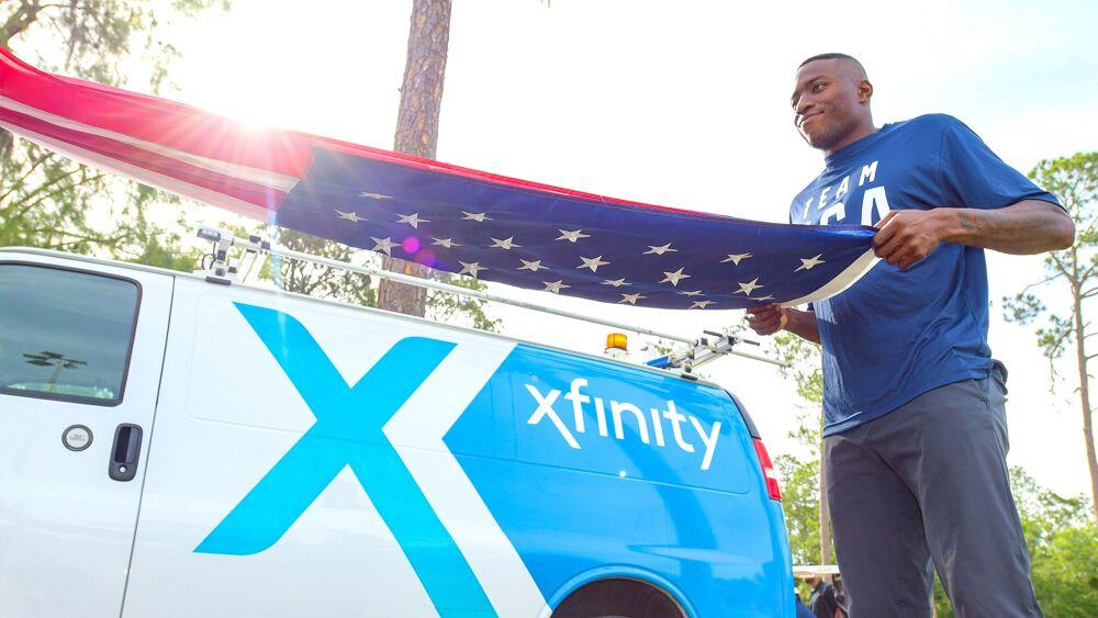 A person folding an american flag. An Xfinity truck to the side.