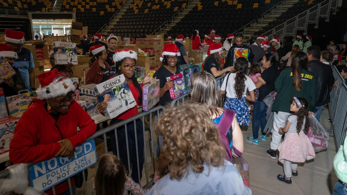 Volunteers in santa hats handing out toys to kids in a large auditorium.