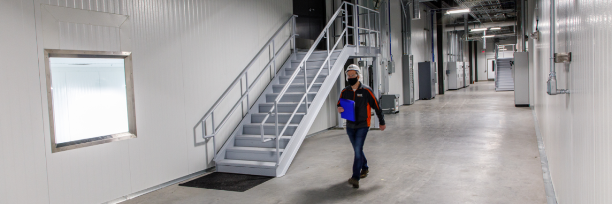 A person walking through a long hallway. A staircase to their right.