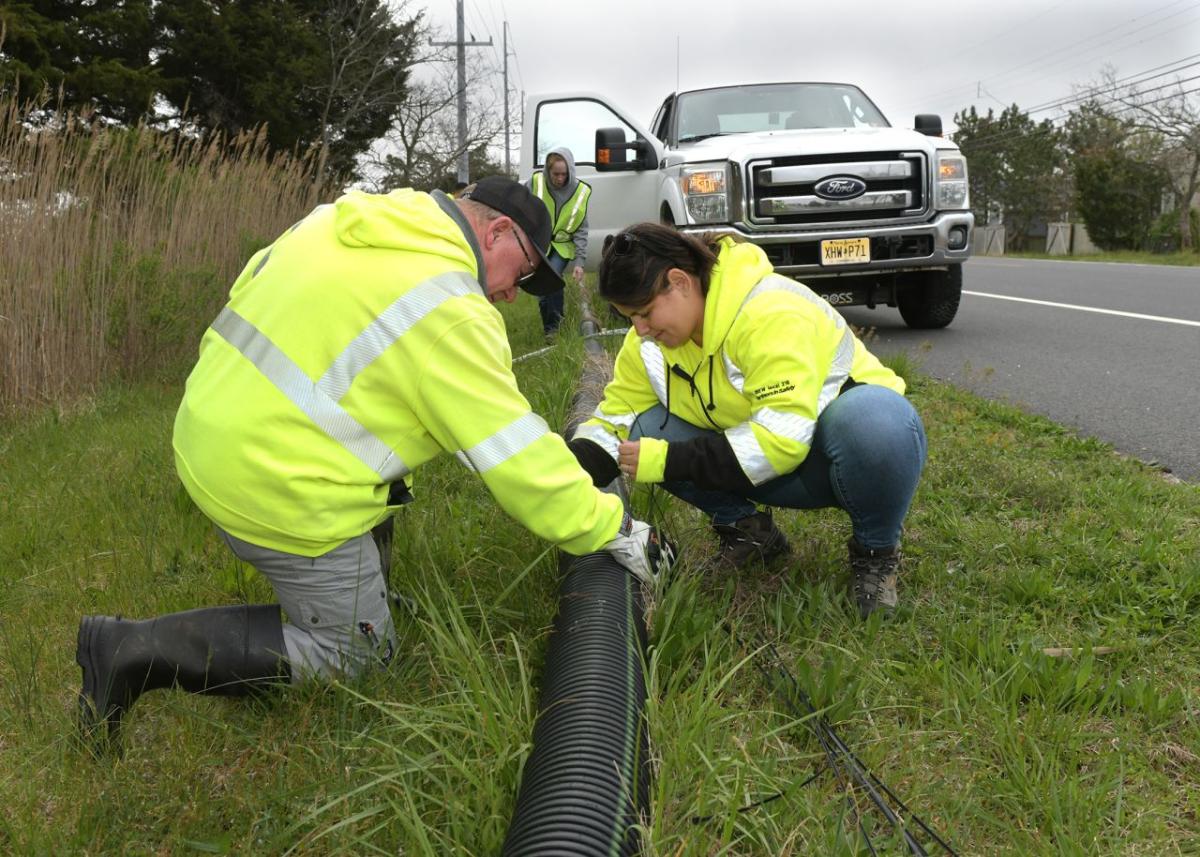 Volunteers working with a drain pipe on the side of a road.