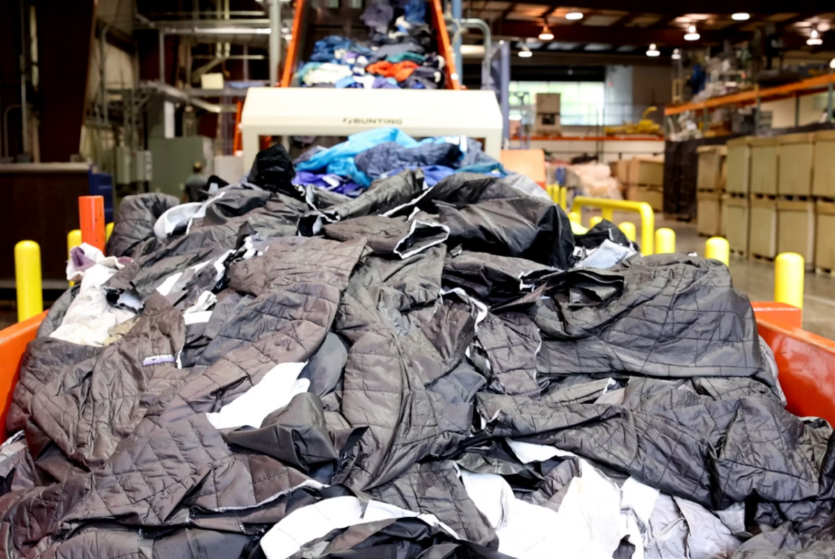 A large pile of waste apparel is loaded onto a conveyor.