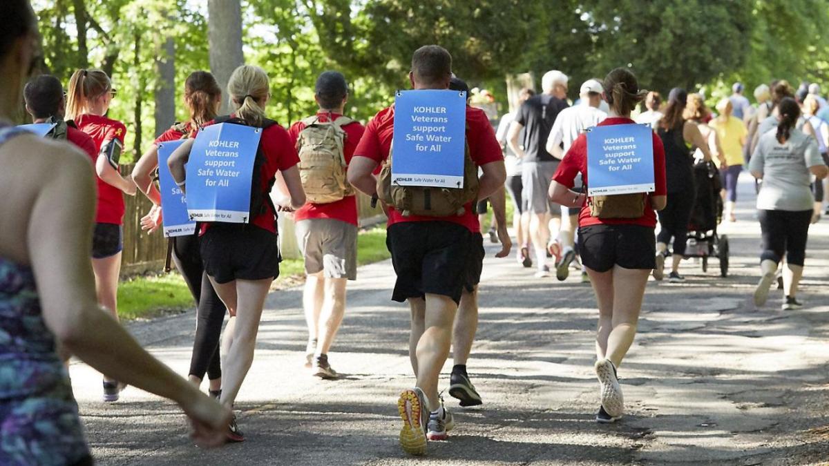 A group of runners with a sign on their back "Kohler veterans support safe water for all".