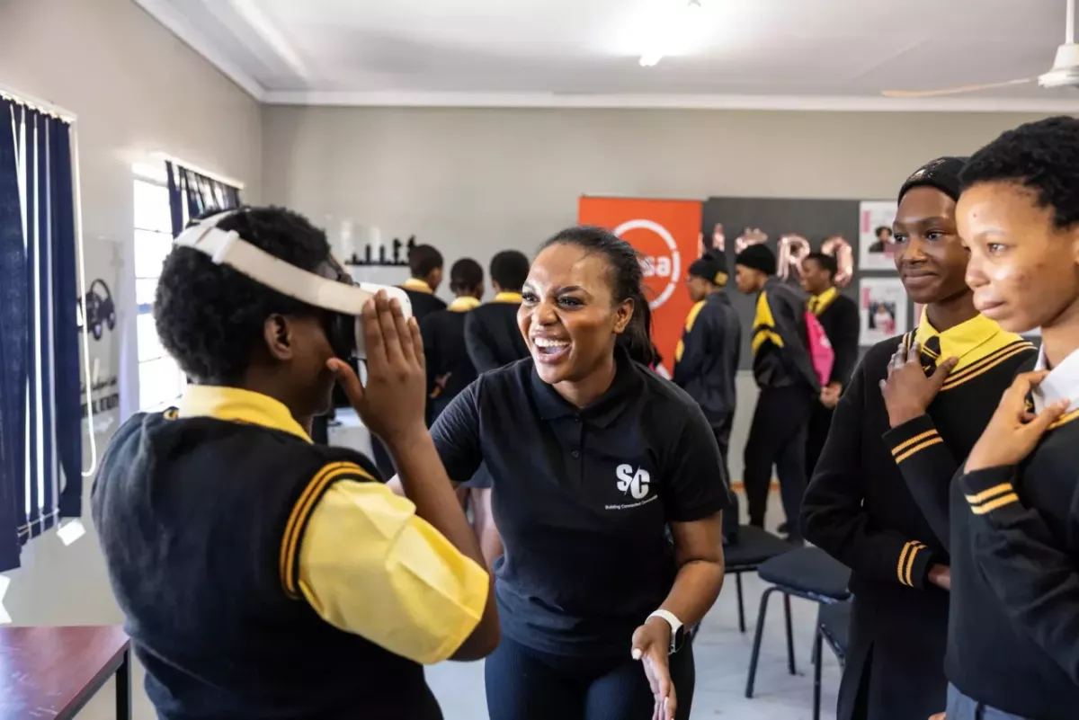 An adult smiles and assists a child with a vr headset. Others look on smiling.