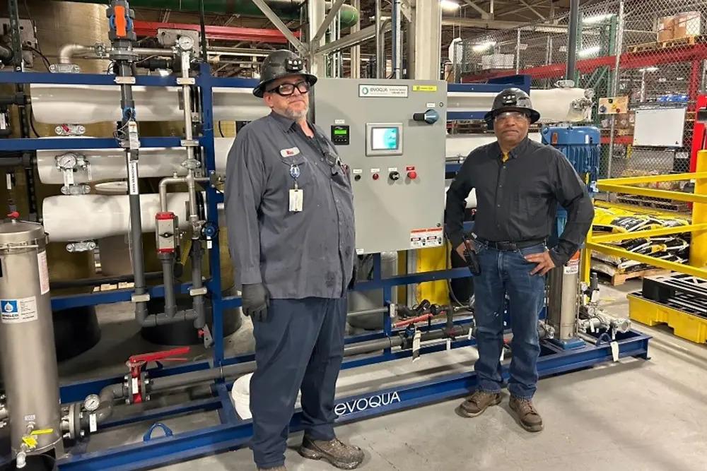 Two people in hard hats standing by a control panel.