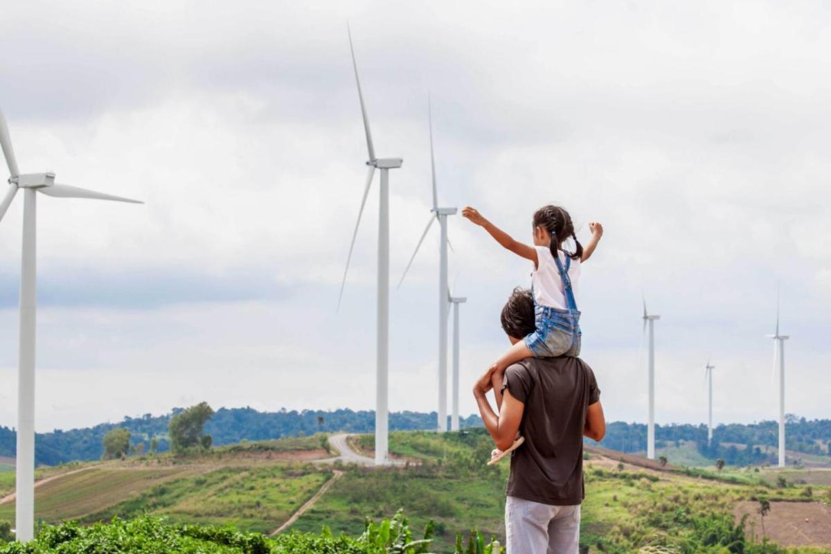 A child one the shoulders of an adult, a row of wind turbines in the distance.