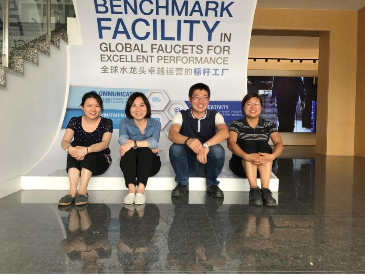 Four people seated in front of a sign "Benchmark facility in global faucets for excellent performance."